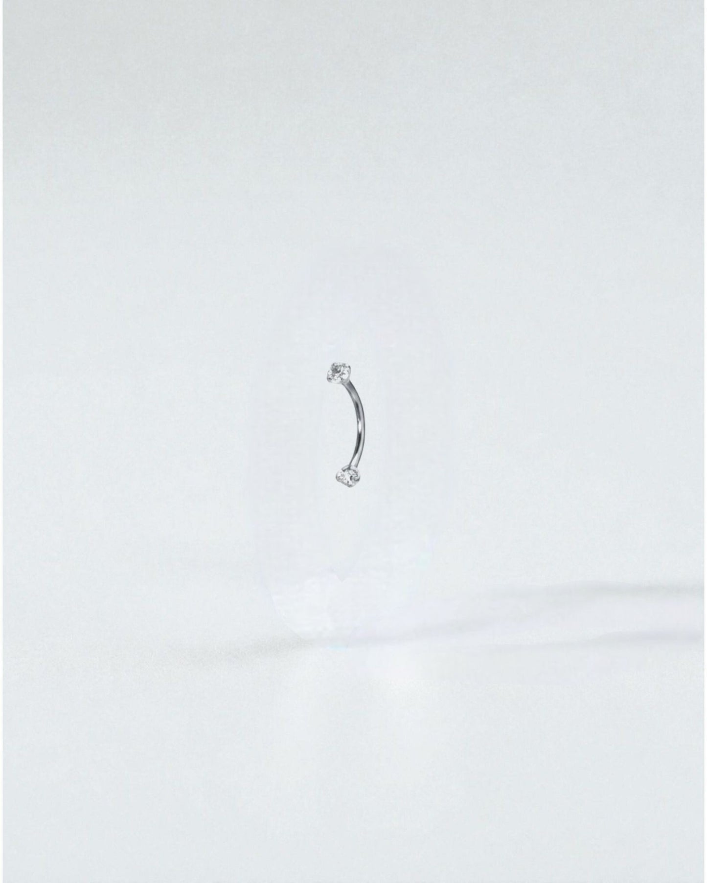 Odonata gold curved barbell with clear cubic zirconia ends, 8mm length, 16G titanium. Ideal for eyebrow piercings.