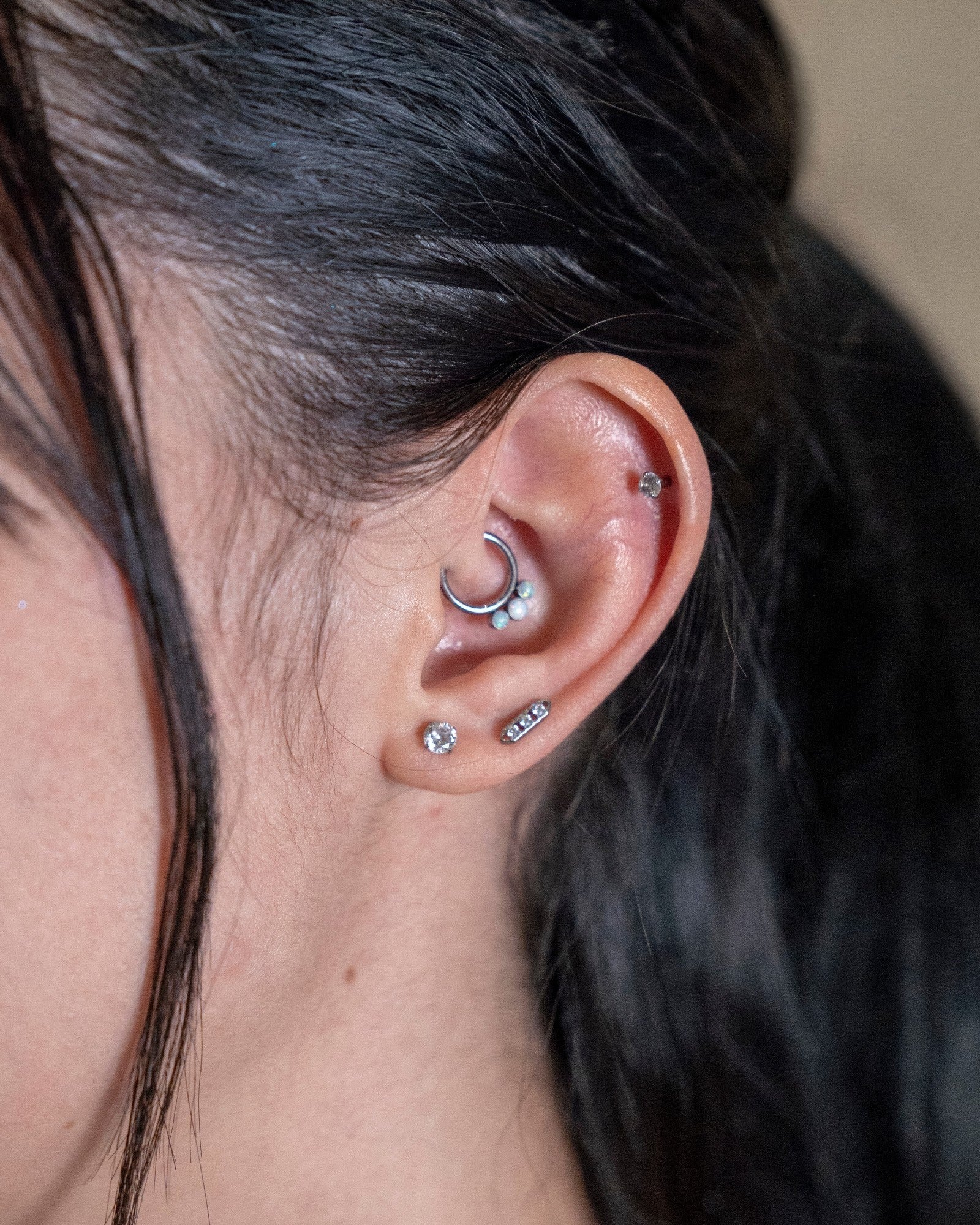 Odonata segment ring with opal accents on a daith piercing. Silver metal hoop with three small white opals.