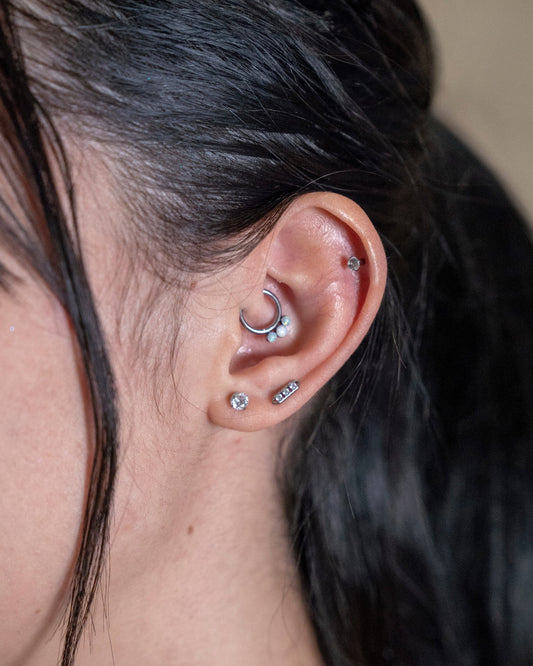 Odonata segment ring with opal accents on a daith piercing. Silver metal hoop with three small white opals.