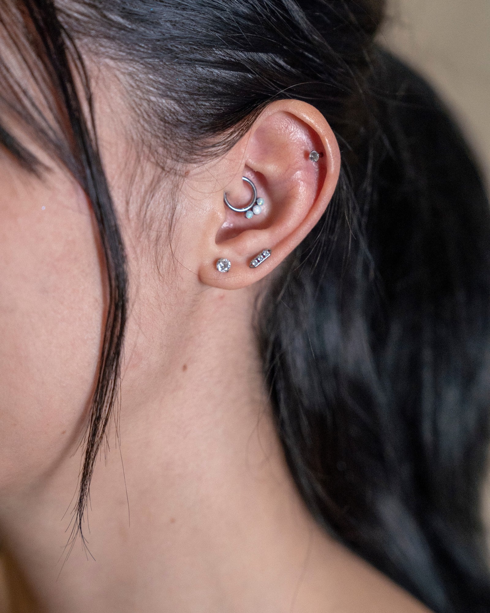 Odonata silver segment ring with three small white stones and a clicker ring with opals in a woman's ear.